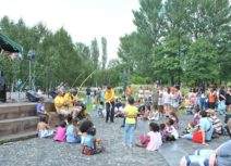 Photo of children and families sitting in Hulme Park watching a theatre performance