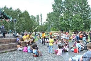 Photo of children and families sitting in Hulme Park watching a theatre performance