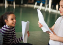 Photo of two children holding pieces of A4 paper and looking at each other smiling