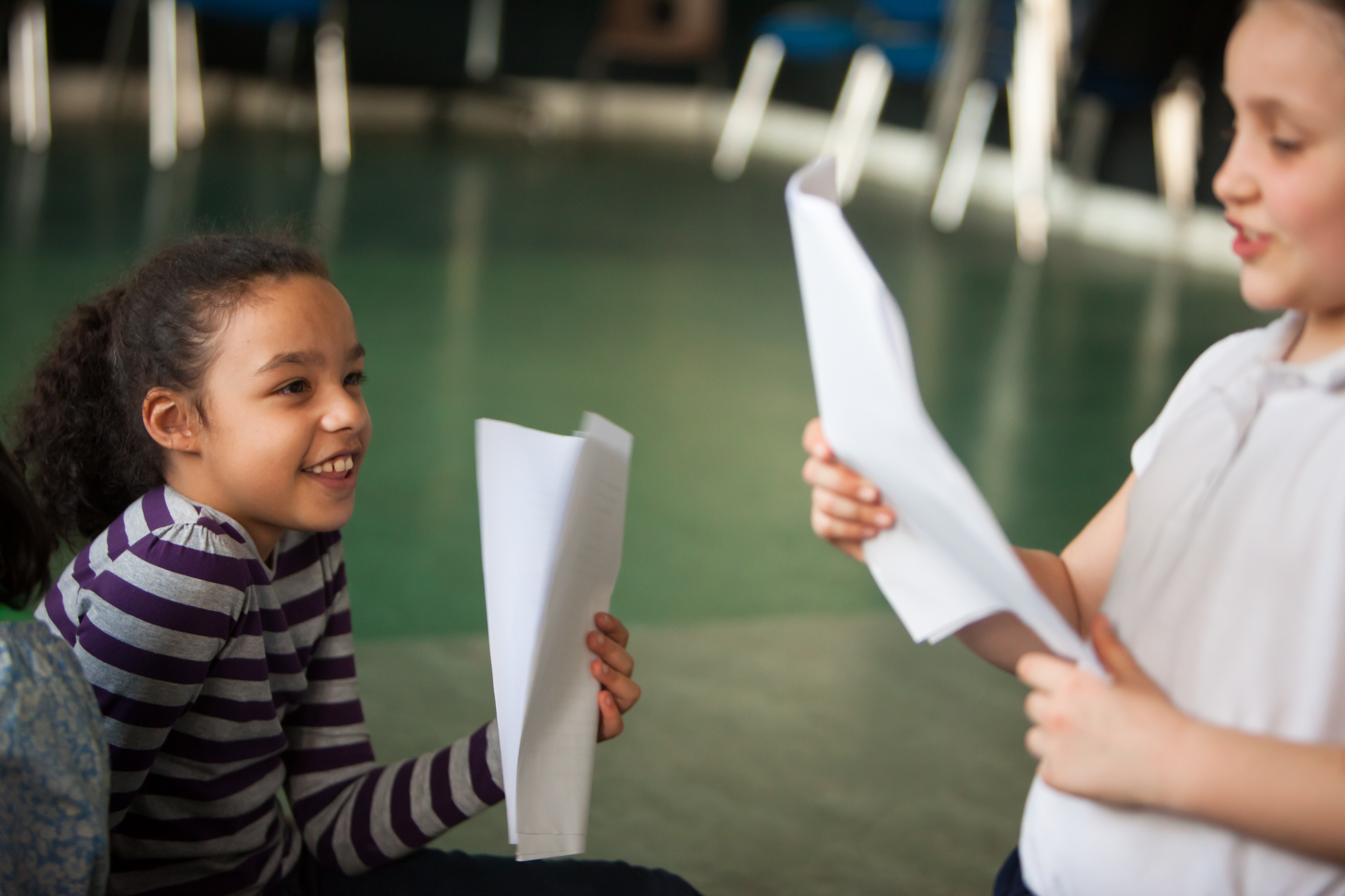 Photo of two children holding pieces of A4 paper and looking at each other smiling