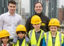 Photo of four children and two adults on Renaker development viewing platform. The children are wearing yellow hi-vis jackets and yellow hard hats.