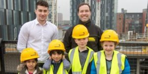 Photo of four children and two adults on Renaker development viewing platform. The children are wearing yellow hi-vis jackets and yellow hard hats.
