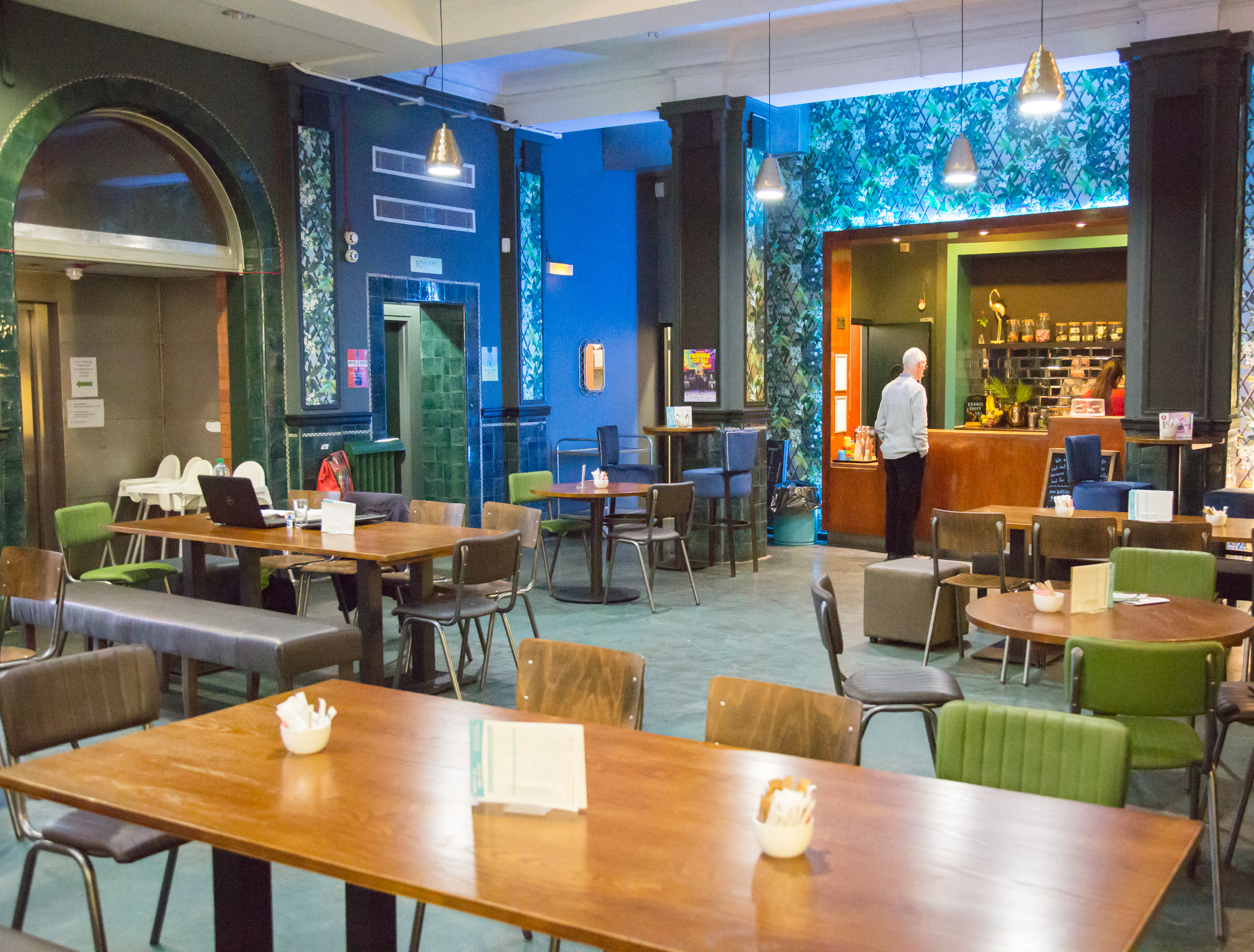 Photo of the interior of Z-café (wooden tables with green leather covered chairs and a blue wall at the far side)