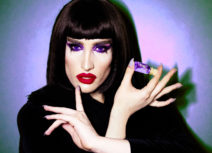 Picture of a woman with black hair, with purple eyes and red lipstick holding a small vial of purple liquid with a cork top.