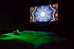 Photo of Z-arts sensory space, a psychedelic pattern is projected onto the wall of a dark space and the floor is illuminated in green