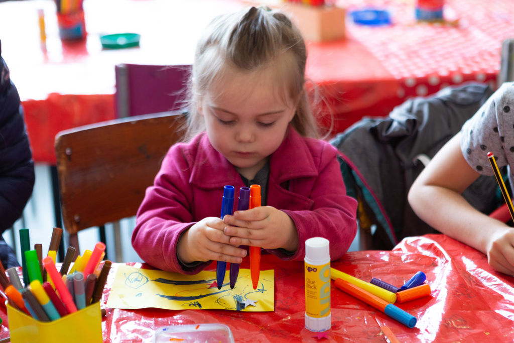 Lead image for Friday Night is Family Night, a young girl wearing a pink jacket is drawing with felt tips on some yellow paper