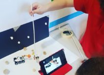 Promotional image for Digital Discoverers - photo from a workshop. Two children are doing stop motion animation - they are recording using a tablet, the scene they have created is a scene on the moon with a spaceman and a space buggy