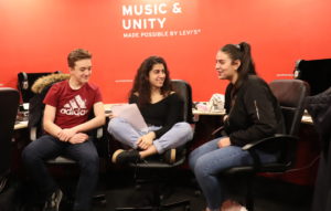 Promo image - Arts and Culture for Teenagers in Manchester - Family Workshop. Two teenage girls and a teenage boy are sat in a room with red painted walls, they are smiling and talking to each other